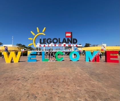 Long shot of very colorful Welcome entrance sign to Legoland(R) California with three young women standing in front of the sign, in the distance.
